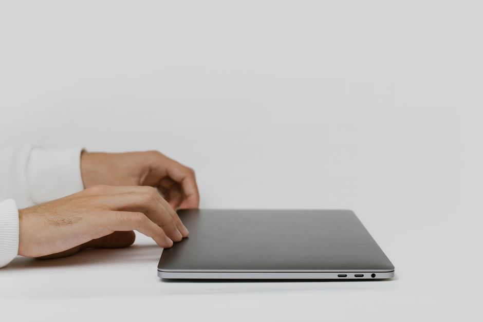 Hands preparing to open a closed laptop on a minimalist desk, ready for work.